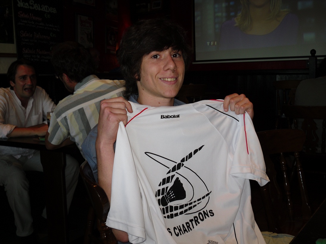 Un jeune homme tenant devant lui un T-shirt blanc avec le logo US chartrons en noir