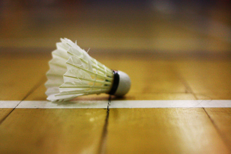 Un volant de badminton posé sur un sol en parquet. Le fond est flou